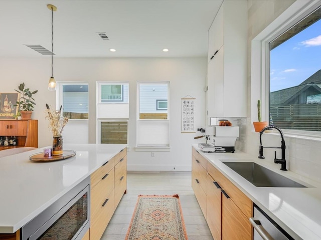 kitchen with sink, appliances with stainless steel finishes, white cabinetry, hanging light fixtures, and light brown cabinetry