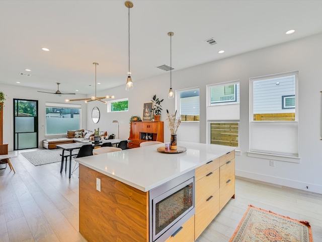 kitchen featuring light brown cabinetry, decorative light fixtures, light wood-type flooring, stainless steel microwave, and a kitchen island