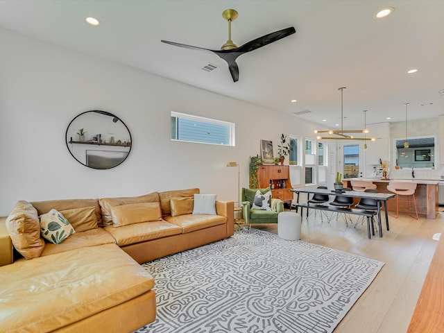 living room featuring ceiling fan with notable chandelier and light wood-type flooring