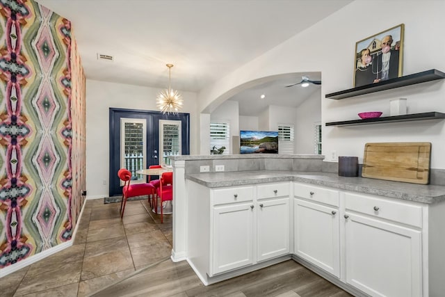 kitchen with kitchen peninsula, hanging light fixtures, white cabinets, french doors, and ceiling fan with notable chandelier