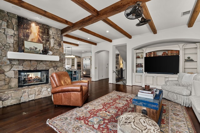 living room with dark hardwood / wood-style floors, beamed ceiling, and a stone fireplace