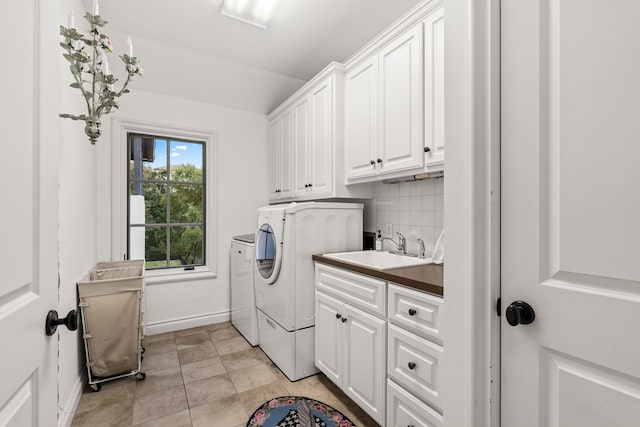 clothes washing area with light tile patterned floors, sink, separate washer and dryer, and cabinets