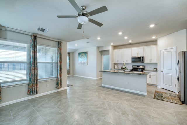 kitchen featuring white cabinetry, stainless steel appliances, tasteful backsplash, a kitchen island with sink, and dark stone countertops