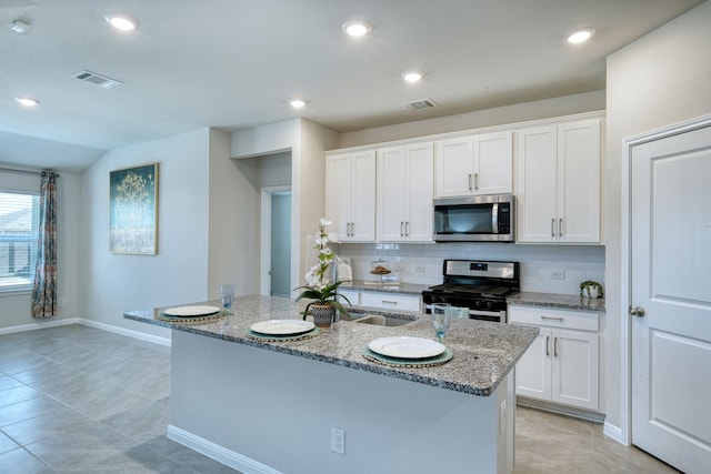 kitchen featuring backsplash, white cabinetry, a center island with sink, and stainless steel appliances