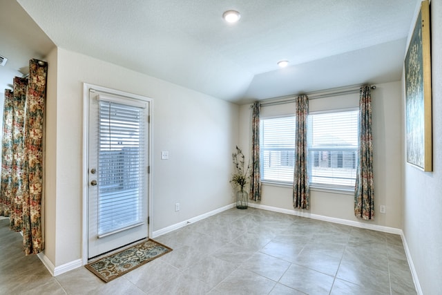 doorway featuring vaulted ceiling and light tile patterned flooring