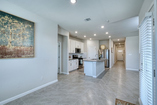 kitchen with light tile patterned floors, white cabinetry, appliances with stainless steel finishes, a kitchen island with sink, and sink