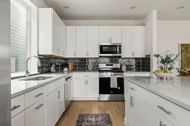 kitchen with appliances with stainless steel finishes, light hardwood / wood-style flooring, white cabinetry, and sink