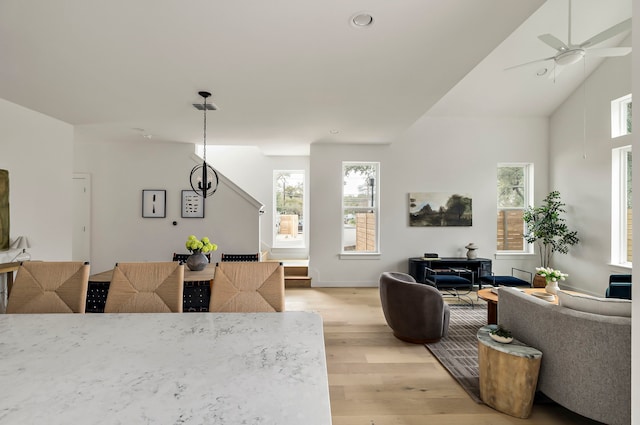 living room with vaulted ceiling, ceiling fan with notable chandelier, and light hardwood / wood-style flooring