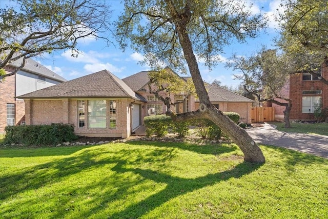 view of front of home with a shingled roof, a front lawn, and brick siding