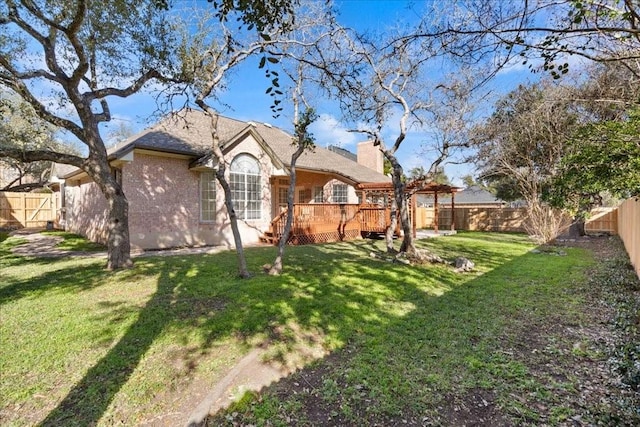 rear view of property with a fenced backyard, a chimney, a yard, a wooden deck, and brick siding