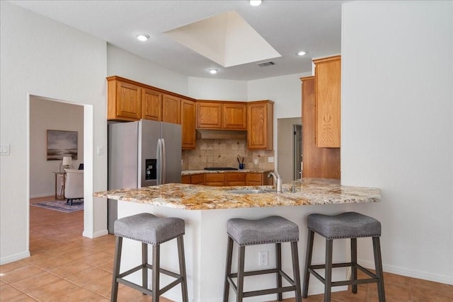 kitchen featuring light tile patterned floors, stainless steel fridge, kitchen peninsula, tasteful backsplash, and sink