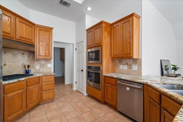 kitchen with light tile patterned floors, appliances with stainless steel finishes, backsplash, and light stone counters