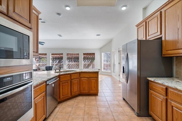 kitchen featuring kitchen peninsula, sink, light tile patterned flooring, light stone countertops, and appliances with stainless steel finishes