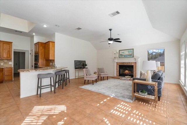 living room with ceiling fan, light tile patterned floors, vaulted ceiling, and a fireplace