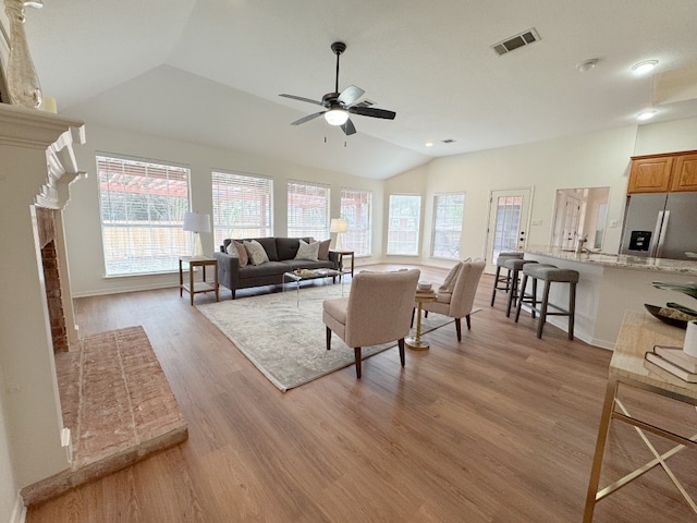 living room with light wood-style floors, a wealth of natural light, visible vents, and lofted ceiling