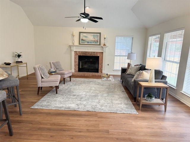 living room featuring lofted ceiling, a tiled fireplace, ceiling fan, wood finished floors, and baseboards