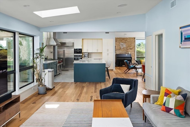 living room with vaulted ceiling with skylight, a wealth of natural light, and light wood-type flooring