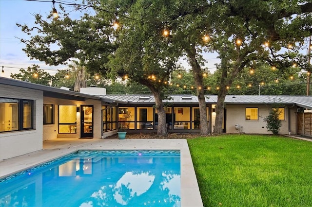 rear view of property featuring an outdoor pool, metal roof, a yard, and a standing seam roof