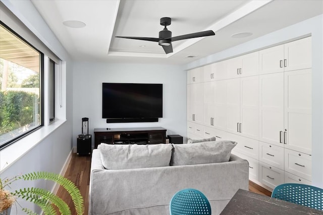 living room with dark wood-type flooring, ceiling fan, and a tray ceiling