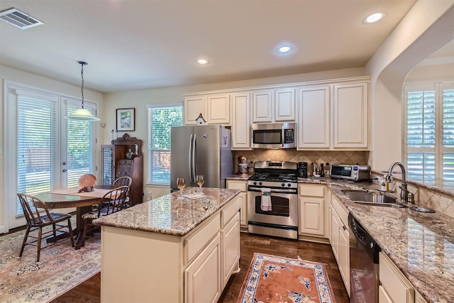 kitchen with stainless steel appliances, decorative light fixtures, light stone countertops, a kitchen island, and sink