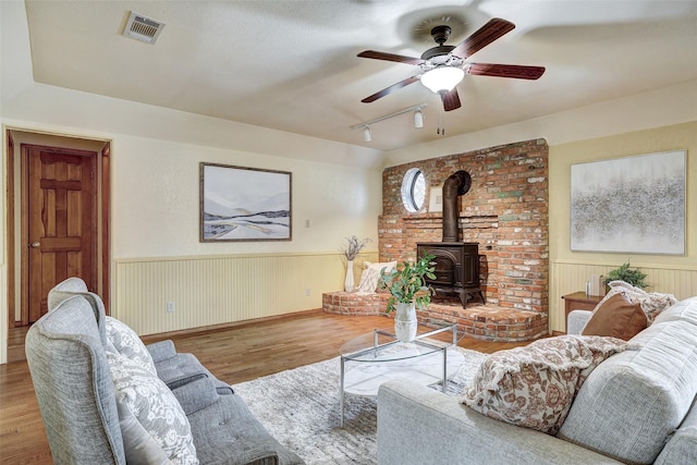 living room with light hardwood / wood-style flooring, track lighting, ceiling fan, and a wood stove