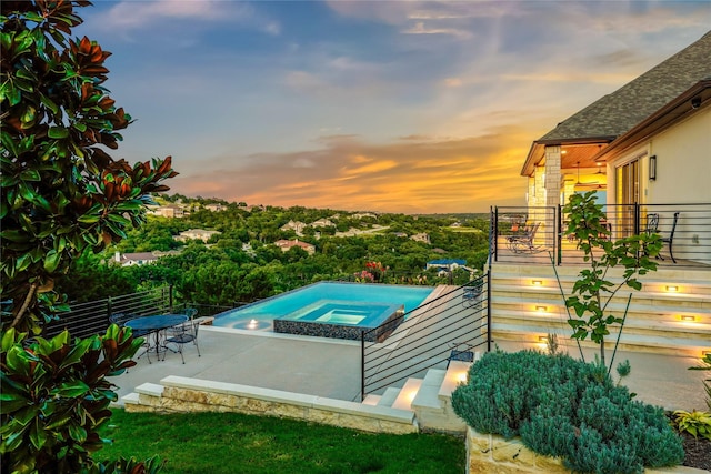 pool at dusk with an in ground hot tub and a patio