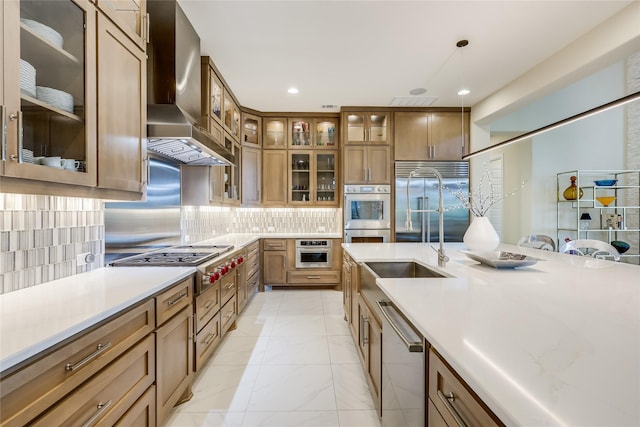 kitchen featuring stainless steel appliances, backsplash, decorative light fixtures, wall chimney exhaust hood, and sink