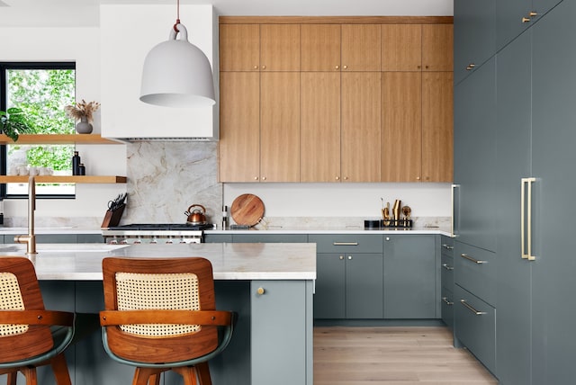 kitchen with light hardwood / wood-style floors, a breakfast bar area, decorative backsplash, hanging light fixtures, and wall chimney range hood