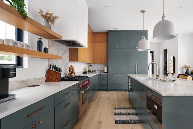 kitchen with light hardwood / wood-style floors, sink, hanging light fixtures, a kitchen island with sink, and high end stainless steel range oven