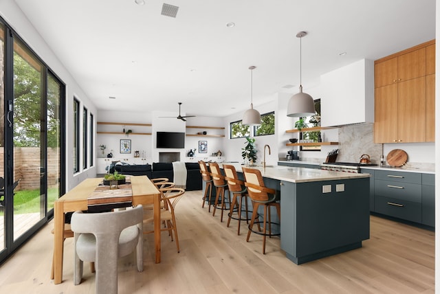 kitchen with decorative light fixtures, gray cabinetry, light wood-type flooring, ceiling fan, and a center island with sink