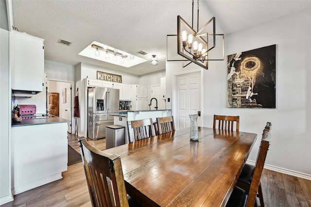 dining area with sink, a textured ceiling, light hardwood / wood-style flooring, and a notable chandelier