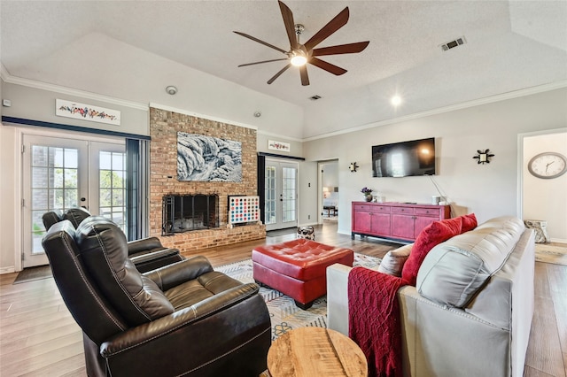 living room featuring a brick fireplace, ceiling fan, a raised ceiling, light wood-type flooring, and french doors