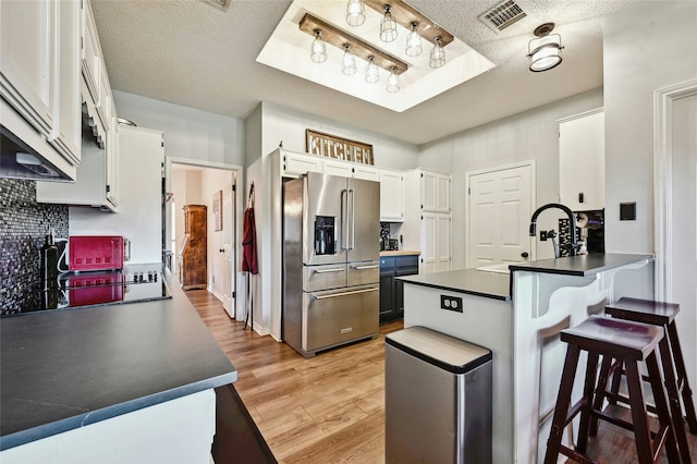 kitchen featuring black electric stovetop, kitchen peninsula, white cabinetry, high end fridge, and a textured ceiling