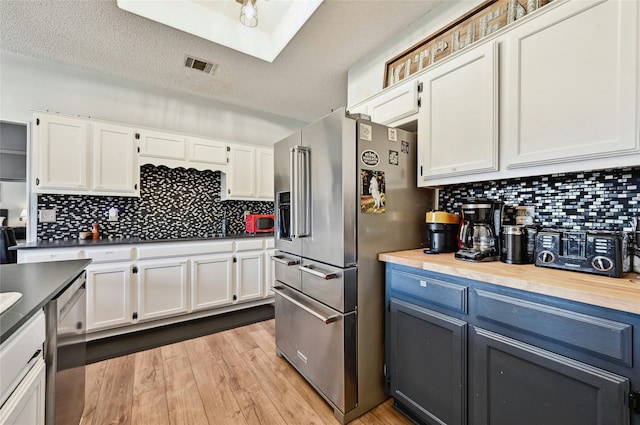 kitchen with light hardwood / wood-style floors, white cabinetry, a skylight, appliances with stainless steel finishes, and a textured ceiling