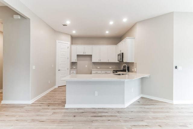 kitchen with light wood-type flooring, kitchen peninsula, appliances with stainless steel finishes, and white cabinetry