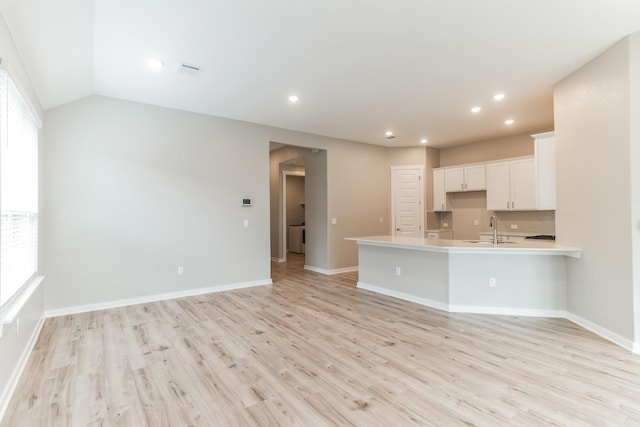 unfurnished living room with light hardwood / wood-style floors, sink, and vaulted ceiling