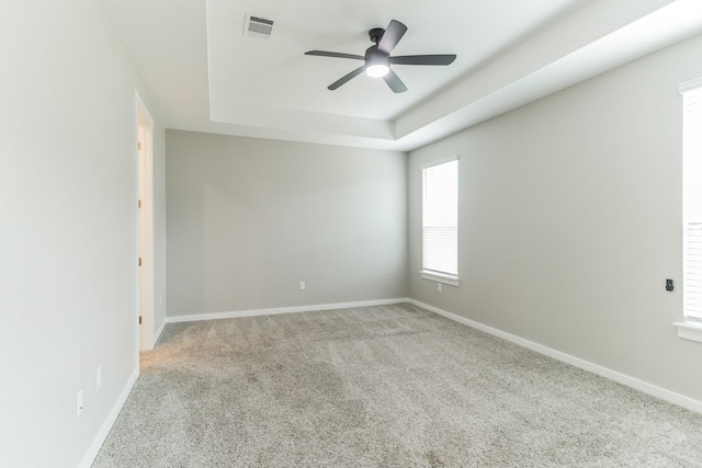 unfurnished room featuring a raised ceiling, ceiling fan, and light carpet