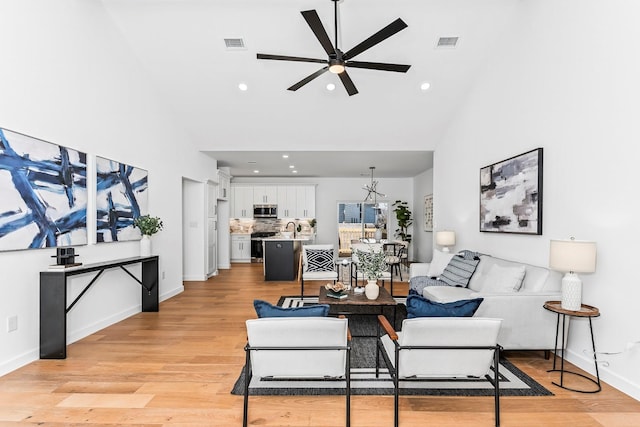 living room with light wood-type flooring, ceiling fan, a towering ceiling, and sink