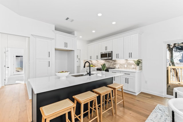 kitchen featuring white cabinetry, light hardwood / wood-style floors, a kitchen bar, a center island with sink, and sink