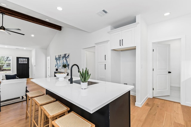 kitchen featuring ceiling fan, a center island with sink, a kitchen bar, sink, and white cabinetry