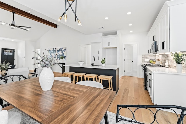 dining area featuring ceiling fan, sink, lofted ceiling with beams, and light wood-type flooring