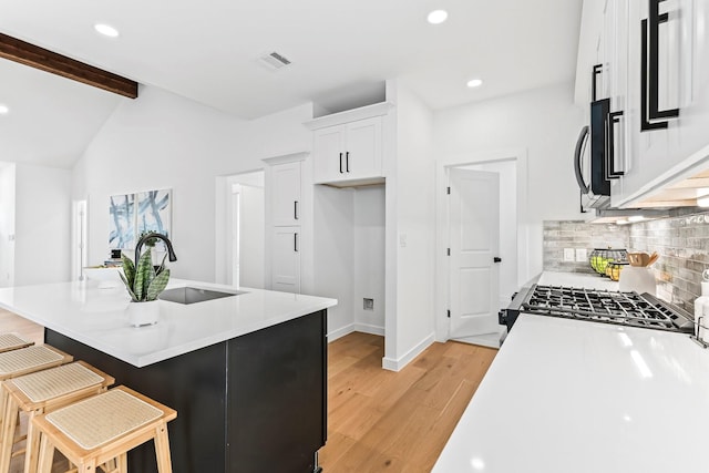 kitchen featuring backsplash, a breakfast bar, sink, white cabinetry, and light hardwood / wood-style flooring