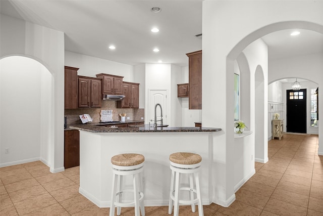 kitchen featuring dark stone counters, tasteful backsplash, sink, kitchen peninsula, and light tile patterned floors