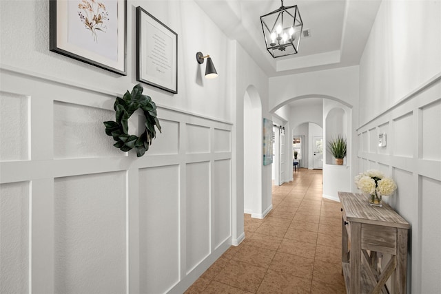 hallway featuring a tray ceiling, light tile patterned floors, and a chandelier