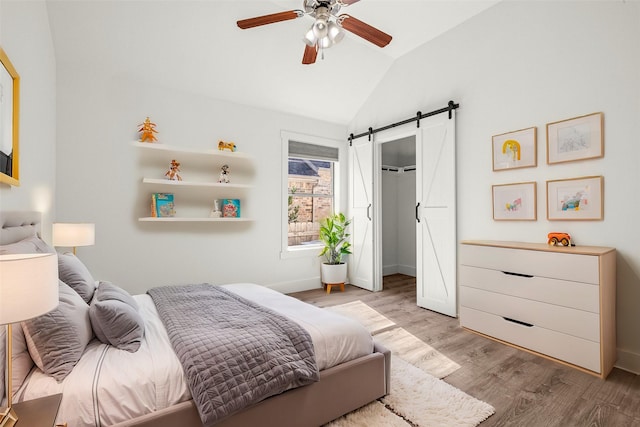 bedroom with vaulted ceiling, ceiling fan, a barn door, and light wood-type flooring