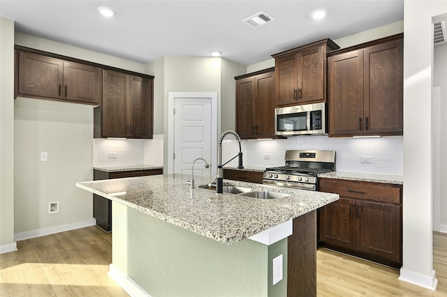 kitchen with light stone counters, visible vents, an island with sink, a sink, and stainless steel appliances