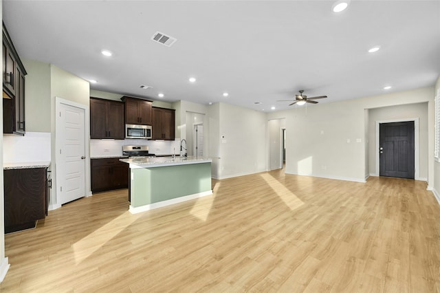 kitchen featuring appliances with stainless steel finishes, light wood-style floors, open floor plan, a kitchen island with sink, and dark brown cabinets