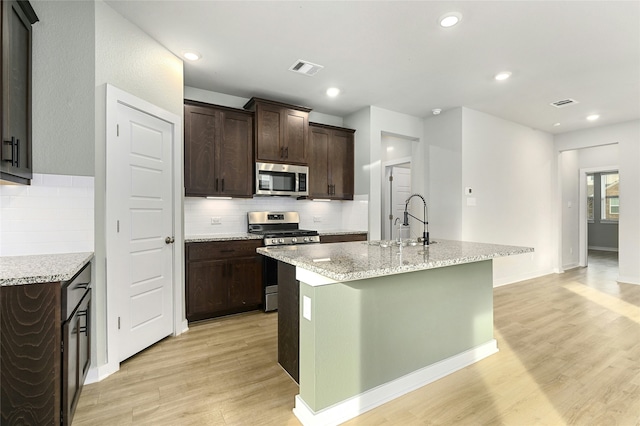 kitchen with visible vents, a kitchen island with sink, stainless steel appliances, dark brown cabinets, and light wood-type flooring