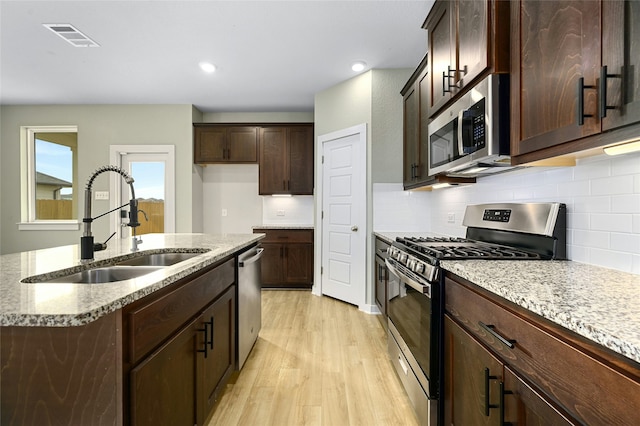 kitchen featuring light stone countertops, visible vents, a sink, light wood-style floors, and appliances with stainless steel finishes