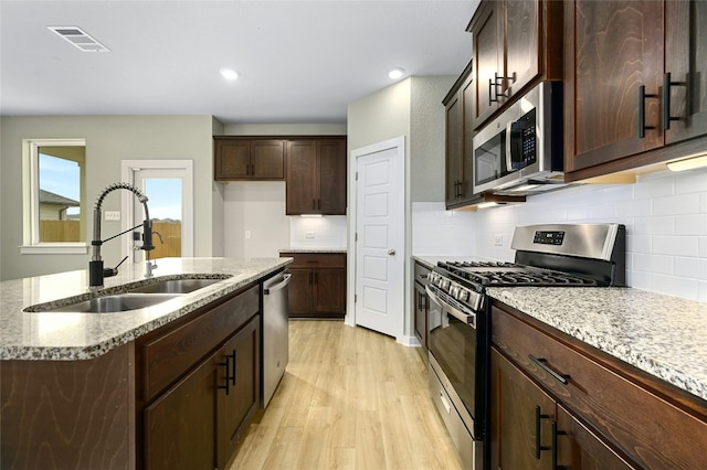 kitchen featuring stainless steel appliances, a sink, visible vents, light wood-style floors, and light stone countertops